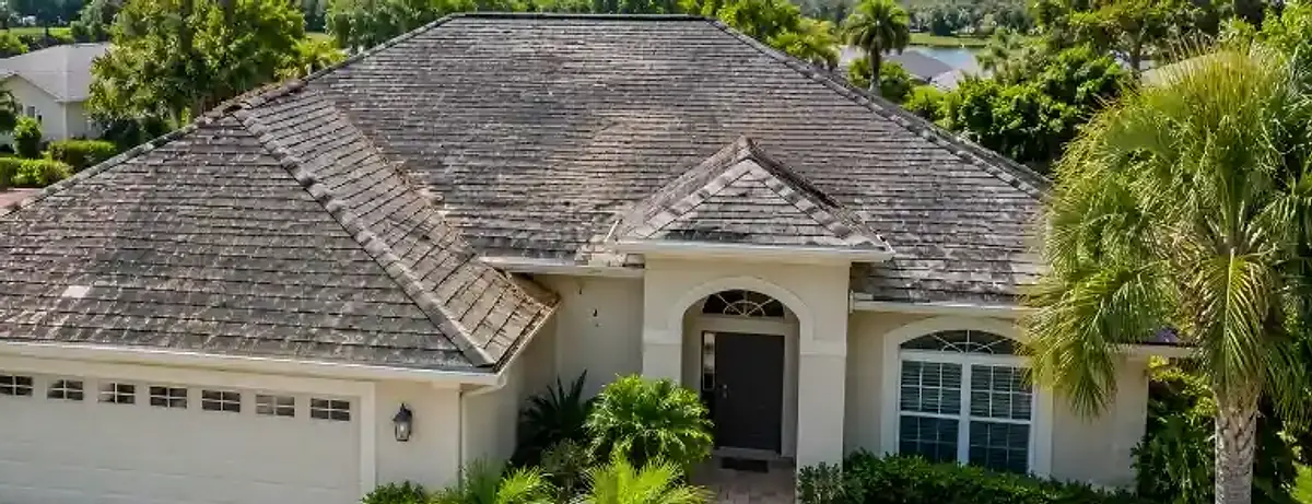 Weathered gray asphalt shingle roof with dark algae stains on a stucco Florida home before roof replacement