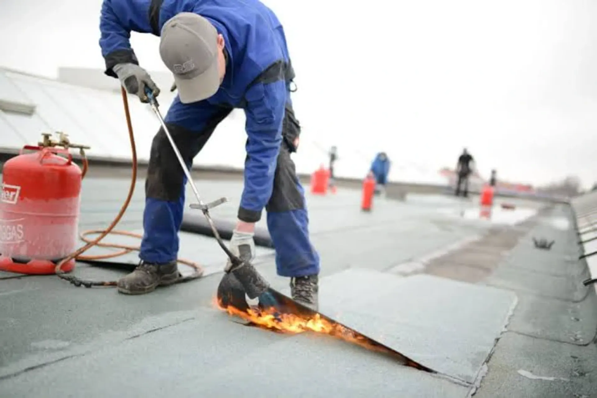 Roofer using a torch to seal a modified bitumen membrane during a flat roof replacement
