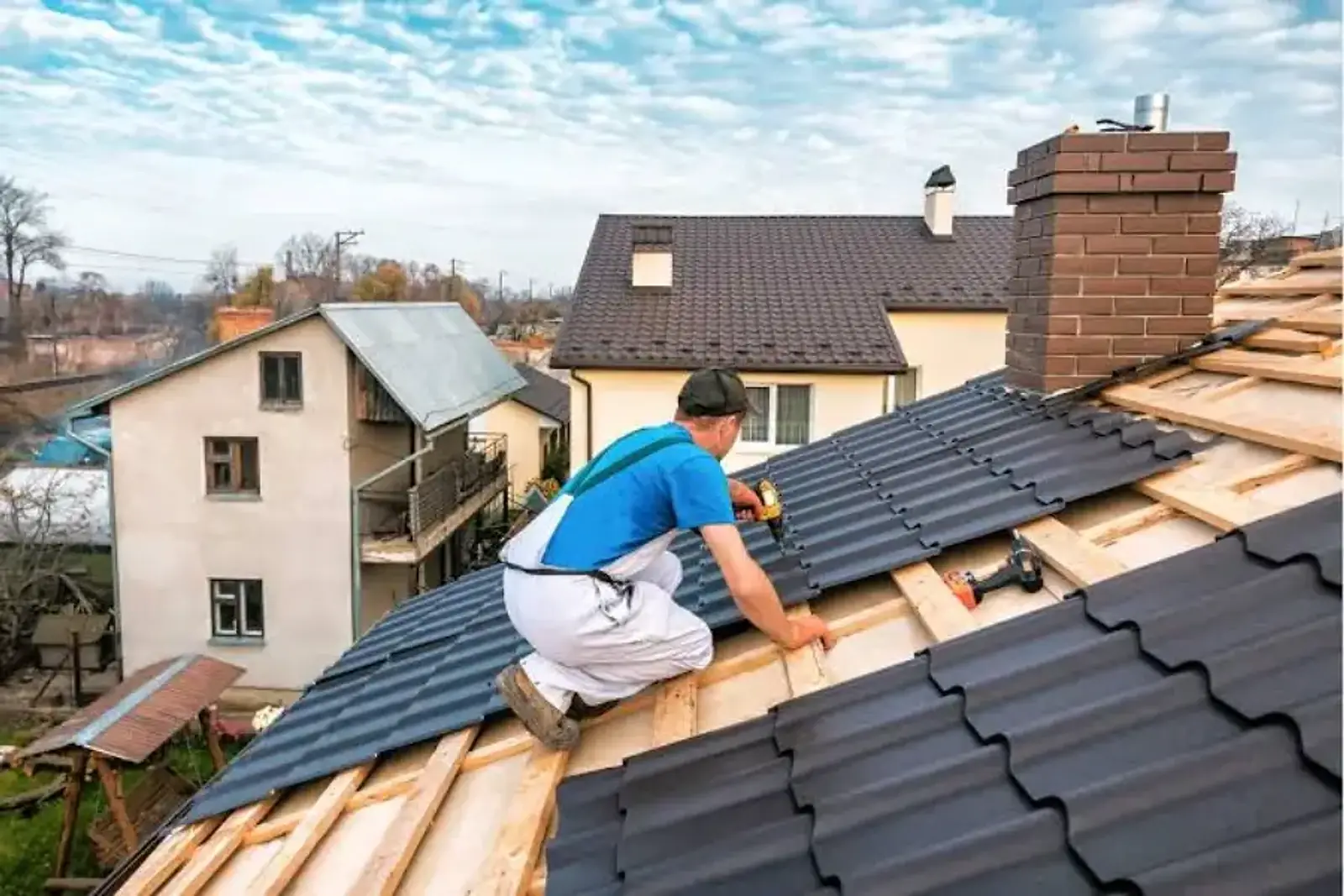 Roofer screwing dark tile-profile metal roofing panels onto wooden battens during a metal roof replacement