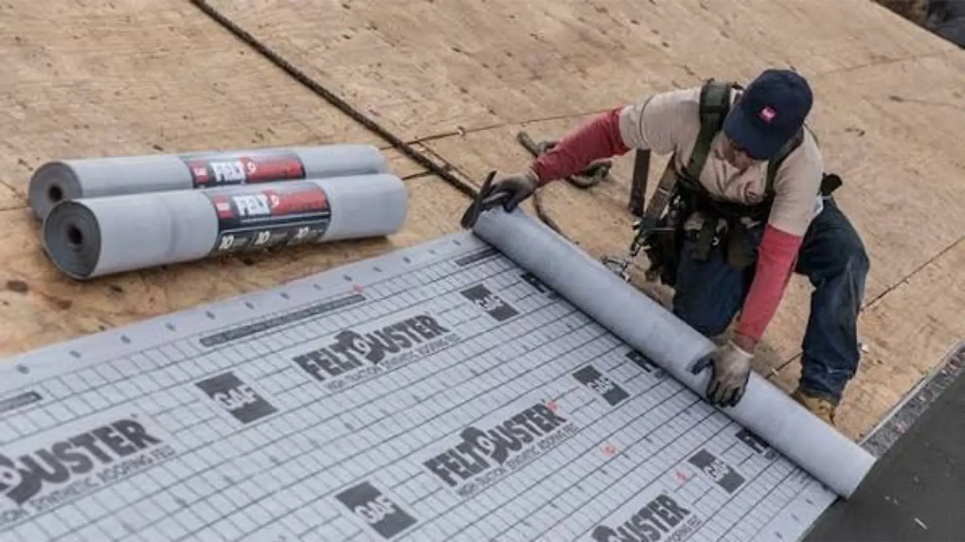 Roofer rolling out synthetic underlayment over a new plywood roof deck during a roof installation