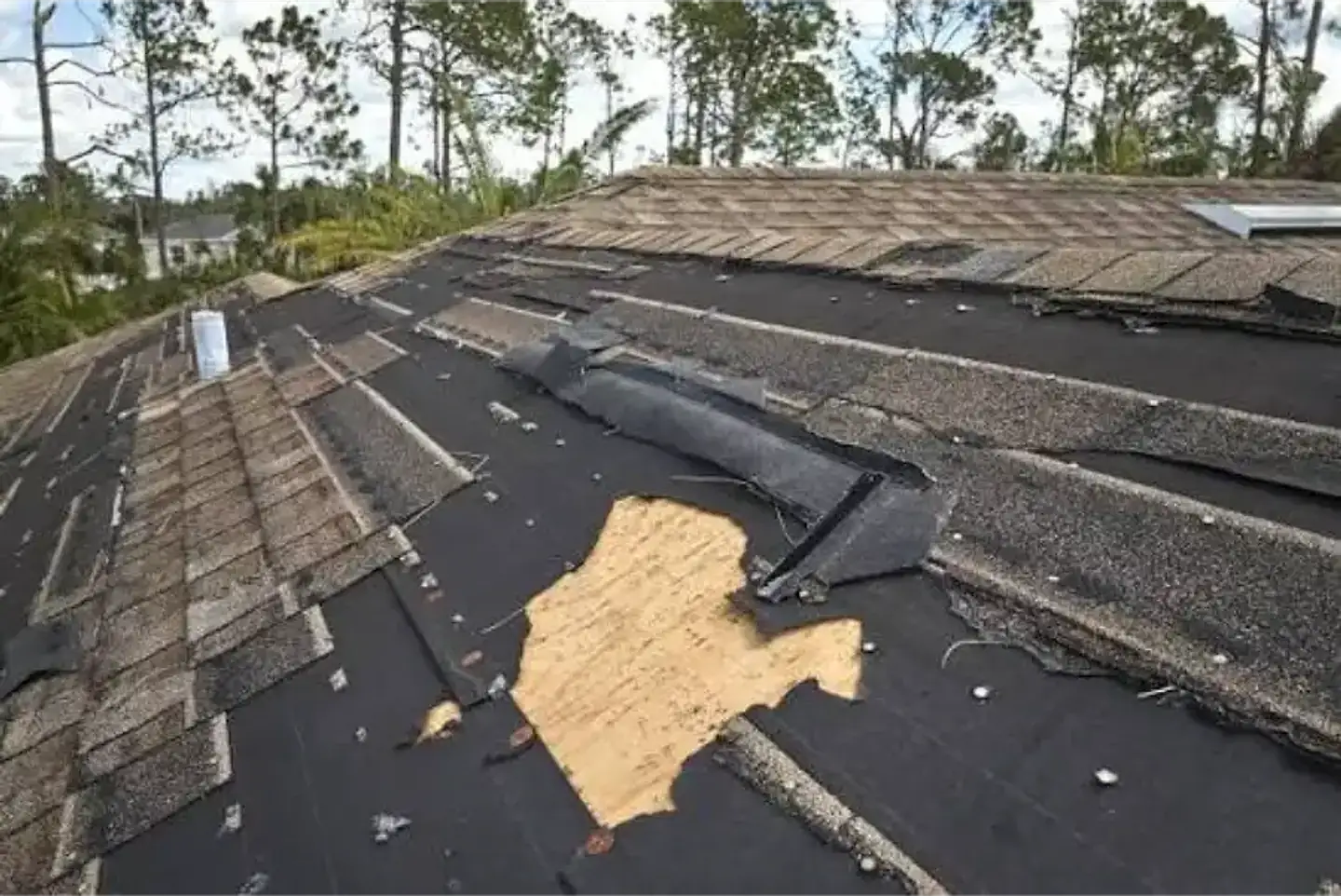 Wind-damaged shingle roof with missing shingles, torn underlayment and exposed plywood decking after a storm